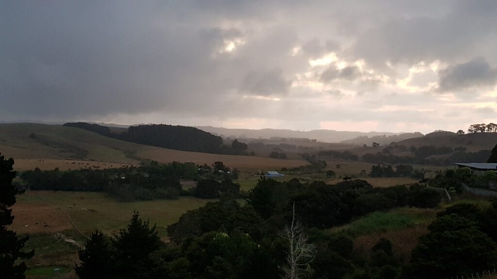 Look across the Kaipara valley with rainclouds in the background and diffuse light coming through the clouds.