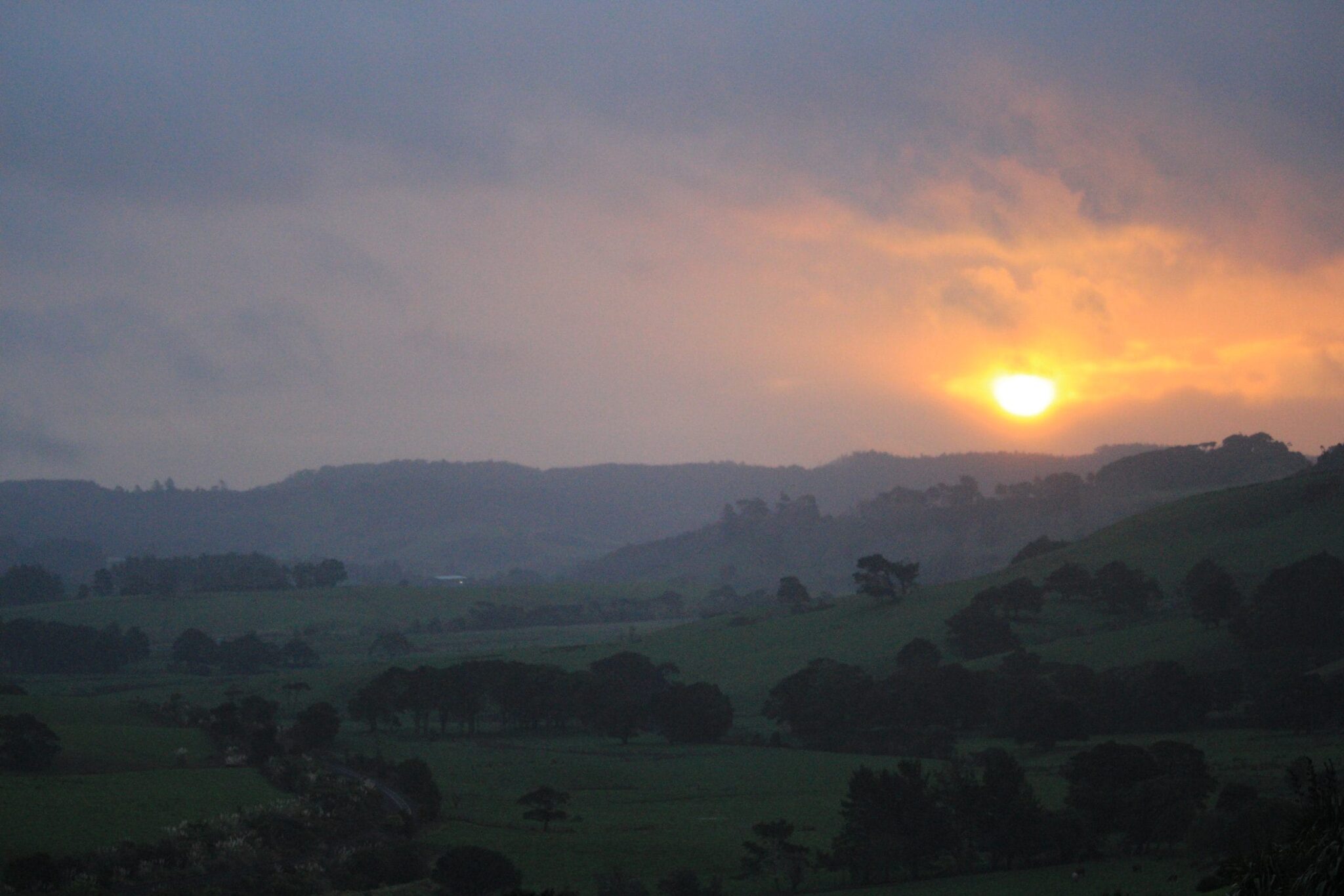 Rainy landscape in misty layers and some sun pushing through thick clouds orange in the background