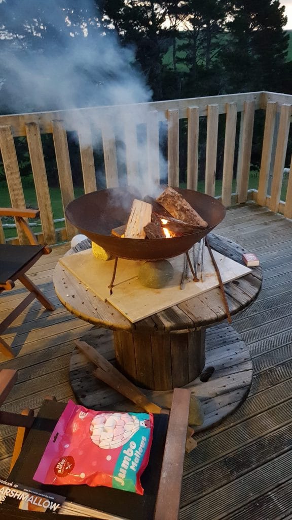 A metal fire bowl with wood stacked up in it, smoking