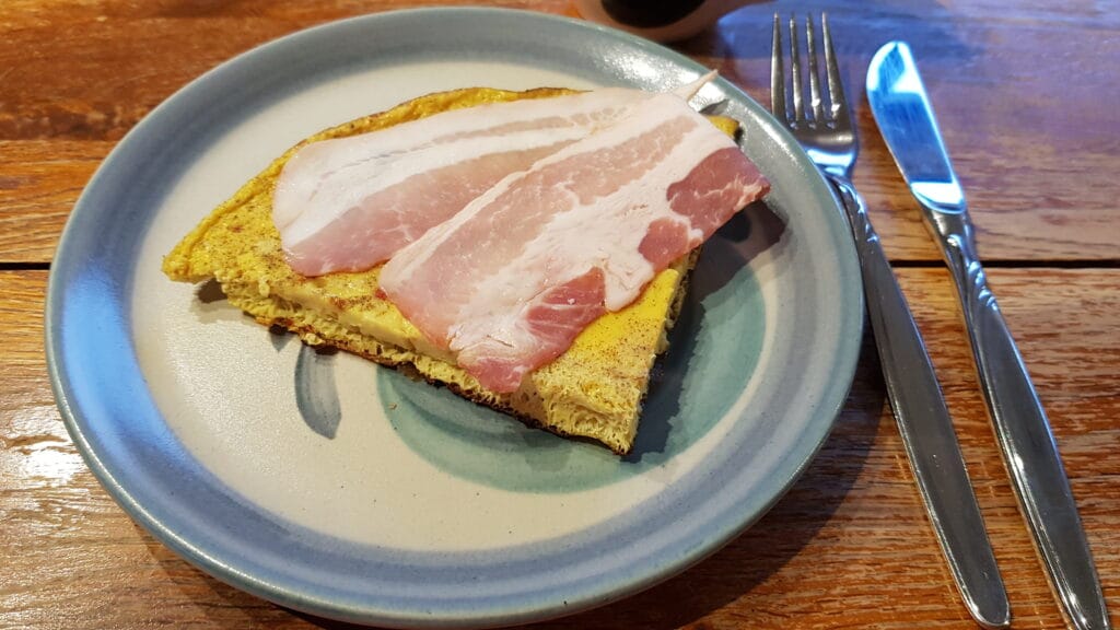 Quarter omelette on a plate with streaky bacon folded on top
