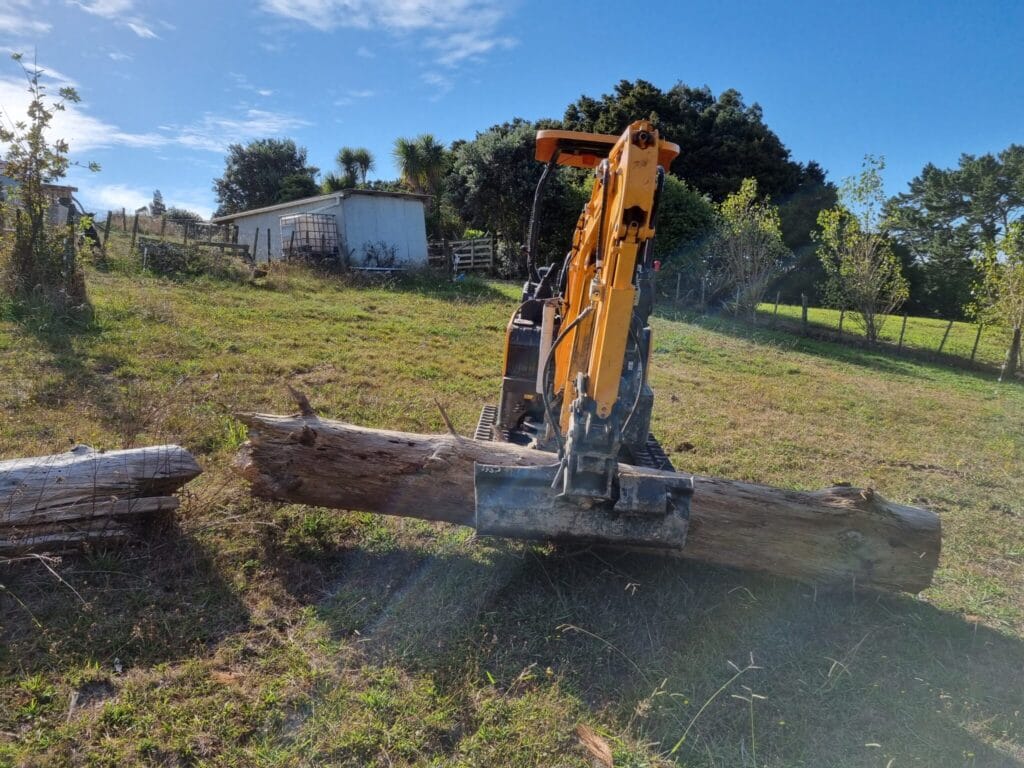 Digger in the paddock with a large log between bucket and blade