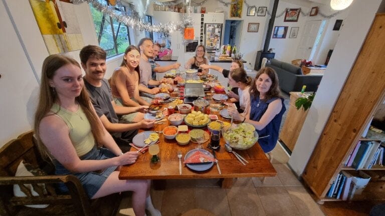 Long table with lots of food on it and lots oof people looking into the camera smiling