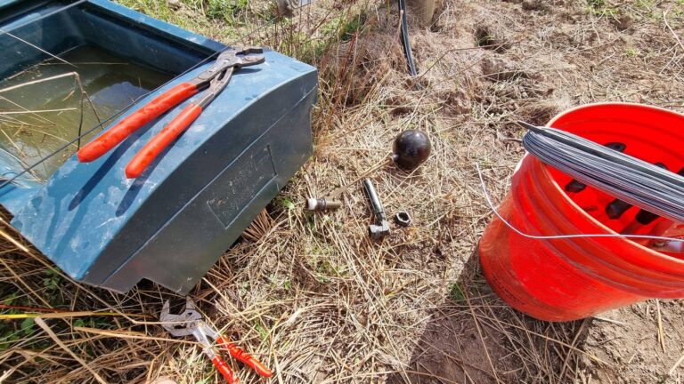 Plastic water trough with spanner on top, some pipe parts next to it and a bucket of tools